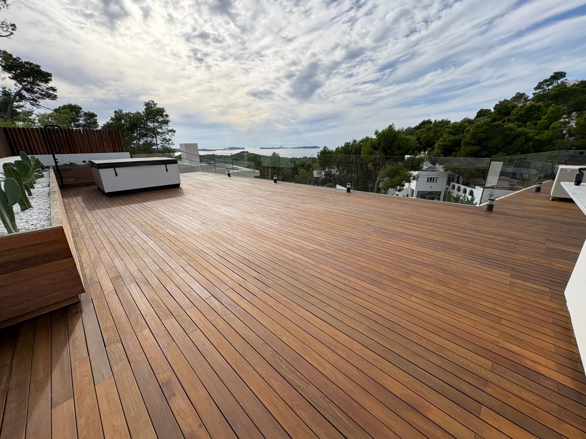 Grande terrasse en bois exotique rénovée, avec garde-corps en verre et vue sur la mer